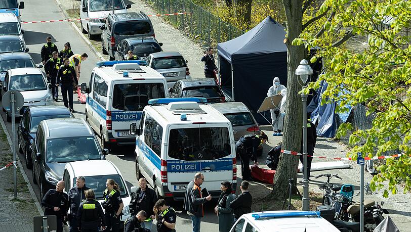 Polizisten und Beamte der Spurensicherung in weißen Schutzanzügen stehen an dem Ort, wo ein toter Mann gefunden wurde.