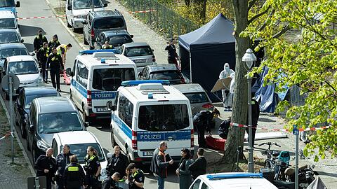 Polizisten und Beamte der Spurensicherung in weißen Schutzanzügen stehen an dem Ort, wo ein toter Mann gefunden wurde.