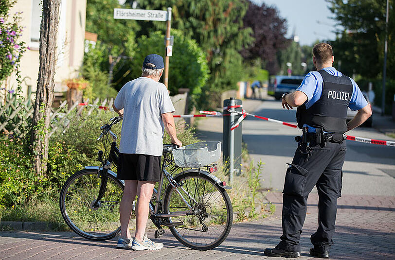 Ein Anwohner und ein Polizist stehen an einer Absprerrung in der Nähe des Tatorts