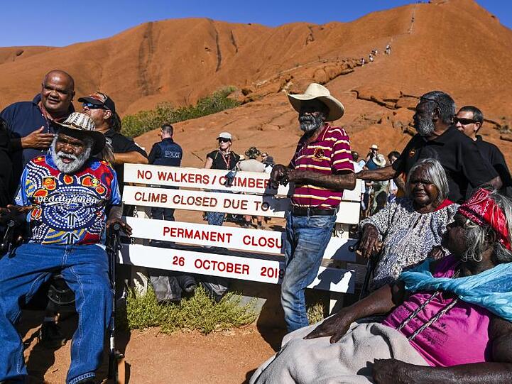 Aborigines-Ureinwohner neben einem neu installierten Schild, mit dem auf die Schließung eines Kletterwegs am Uluru hingewiesen wird.