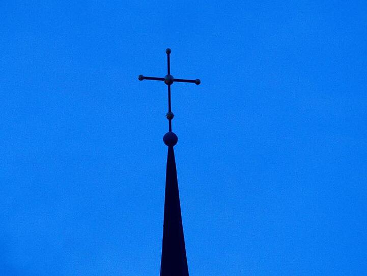Ein Kreuz ist auf einer Kirchturmspitze zu sehen. Foto: Friso Gentsch/dpa/Symbolbild