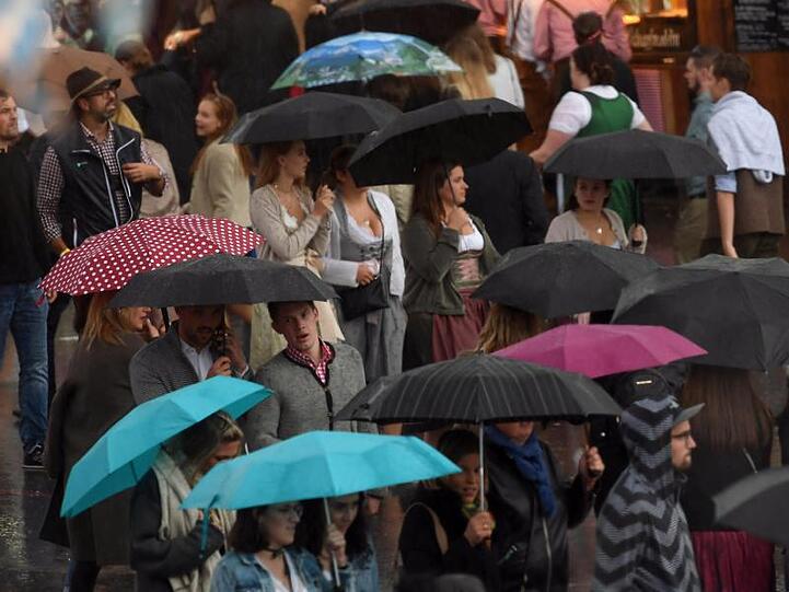 Besucher gehen bei starkem Regen über die Wiesn. Foto: Felix Hörhager/dpa