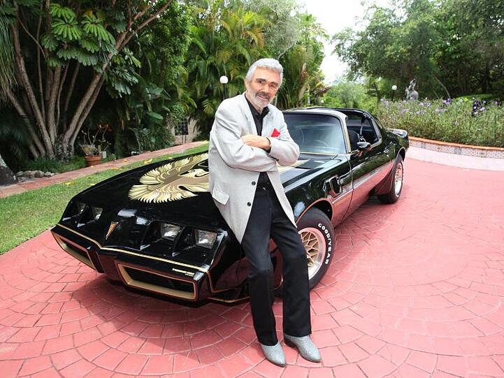 Schauspielers Burt Reynolds steht an seinem schwarz-goldenen Sportwagen der Marke Pontiac Trans Am (1979). Das Auto gehört zu Filmmemorabilien, Kleidungsstücken und Möbeln aus dem Privatbesitz des Schauspielers, die am 15. und 16. Juni in Beverly Hills versteigert werden.