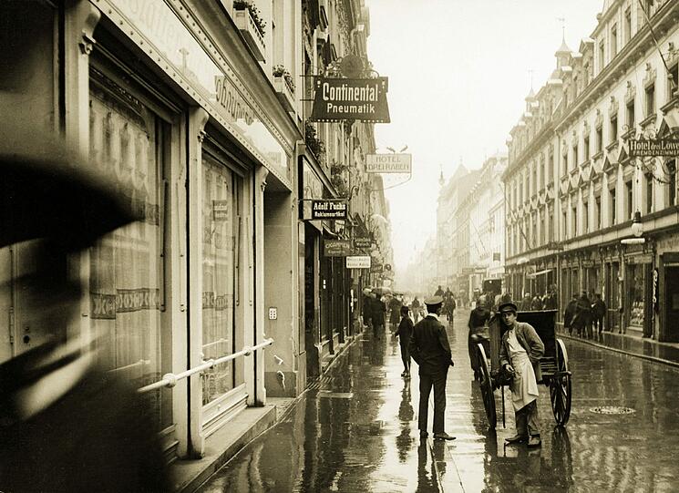 Continental Pneumatik, Hotel Drei Raben, Adolf Fuchs Reklameartikel, Schirm-Fabrik Welsch, Friseure: Die Geschäftswelt der vom Regen glänzenden Schillerstraße im Jahr 1905.