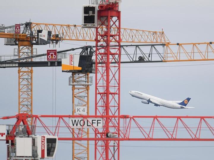 Eine Passagiermaschine der Lufthansa startet auf dem Frankfurter Flughafen hinter Baukränen.