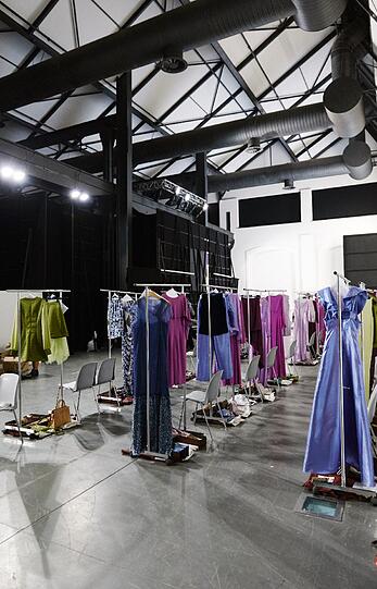 Die Ruhe vor dem Show-Sturm: In Reihen sind backstage die Wechselklamotten für die Models aufgebaut. Neben jedem Outfit liegen Schmuck, Taschen und Schuhe bereit. Jeweils zwei Anziehhilfen kleiden ein Model um.