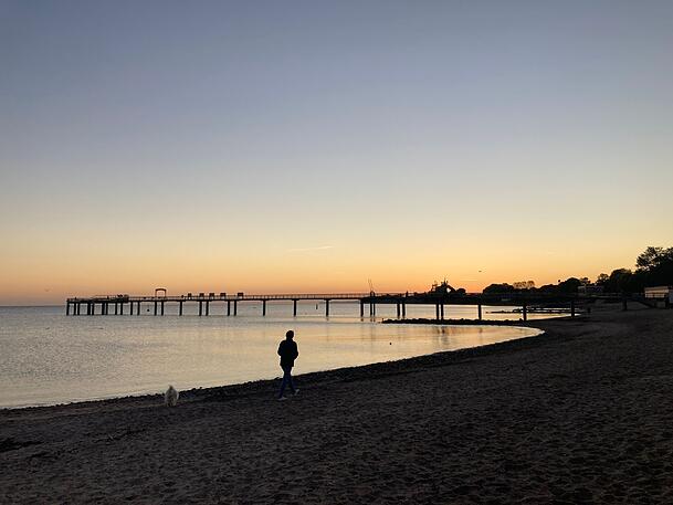 Eine Frau spaziert im Sonnenaufgang am Strand im schleswig-holsteinischen Niendorf entlang.