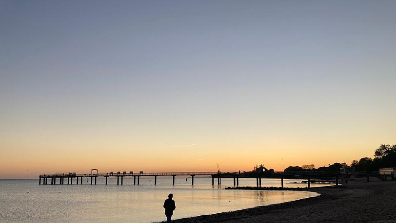 Eine Frau spaziert im Sonnenaufgang am Strand im schleswig-holsteinischen Niendorf entlang.