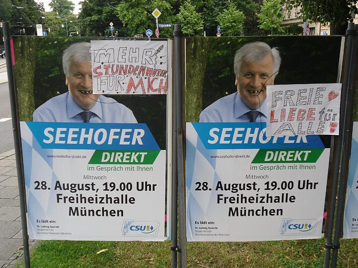 Rechteckige Zusatzaufkleber spielen auf Seehofers Dreiecksbeziehung an.