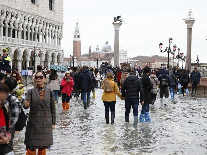 Touristen laufen auf dem überfluteten Markusplatz durch das Wasser.