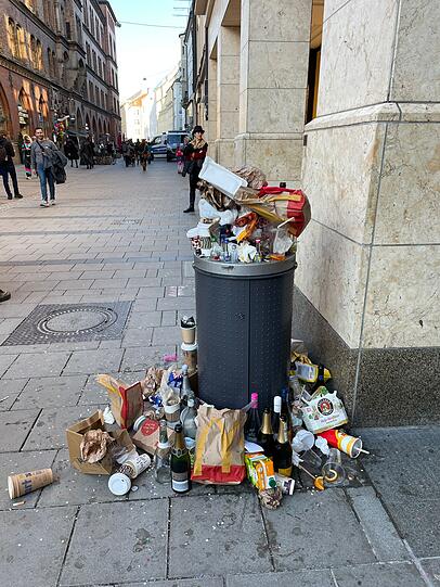 Viele Glasflaschen stehen um den überfüllten Mülleimer herum.