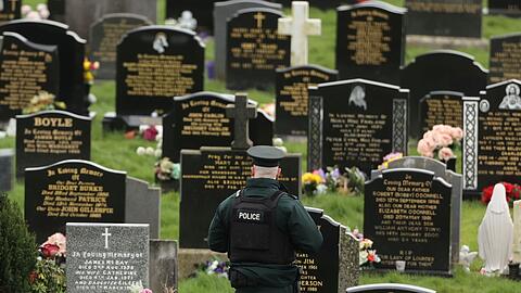 Ein PSNI-Polizist patrouilliert auf dem Stadtfriedhof von Londonderry. Kurz vor der Ankunft von US-Präsident Biden in Nordirland fand die Polizei dort vier mutmaßliche Rohrbomben.