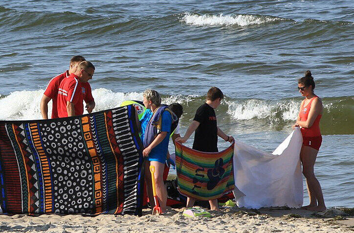 ettungskräfte versuchen am 09.07.2013 am Strand von Trassenheide auf der Insel Usedom einen Mann nach einem Badeunfall zu reanimieren während Helfer mit Decken und Handtüchern den Blick auf den Leblosen abschirmen.