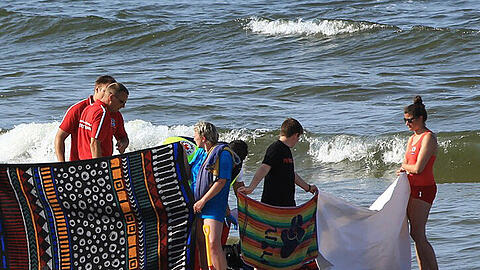 ettungskräfte versuchen am 09.07.2013 am Strand von Trassenheide auf der Insel Usedom einen Mann nach einem Badeunfall zu reanimieren während Helfer mit Decken und Handtüchern den Blick auf den Leblosen abschirmen.