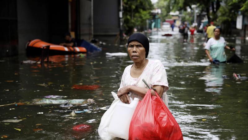 Eine Frau geht durch das Hochwasser einer überfluteten Straße in Jakarta. Eine Frau geht durch das Hochwasser einer überfluteten Straße in Jakarta.