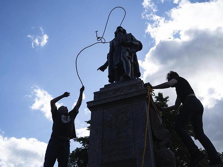 Zwei Männer befestigen ein Seil um den Hals einer Statue von Christopher Columbus.