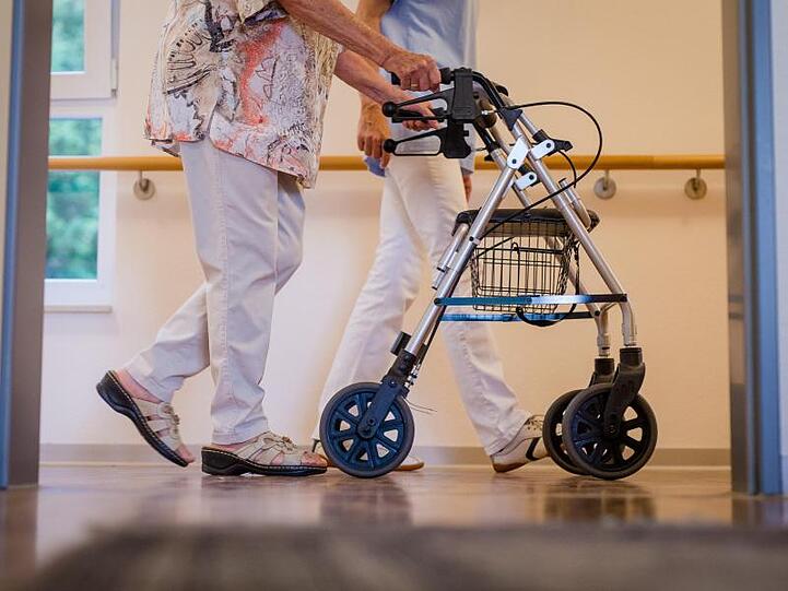 Eine Pflegekraft geht mit einer älteren Frau über einen Korridor in einem Pflegeheim. Der Mindestlohn für mehr als eine Million Pflegekräfte in Deutschland wird erhöht.