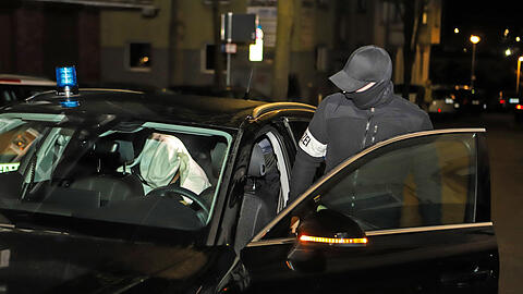 Ein Polizist steigt während einer Razzia in ein Auto in dem eine festgenommene Person sitzt (Symbolbild)