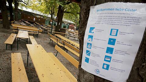 Ein Hinweisschild mit Corona-Restriktionen im Oktober 2020 am Baum eines leeren Biergartens.