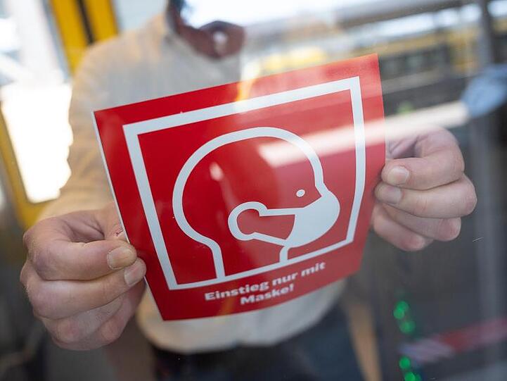 Ein Mann befestigt ein Informationsschild zur Maskenpflicht:. Foto: Sebastian Gollnow/dpa/Symbolbild