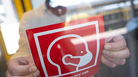 Ein Mann befestigt ein Informationsschild zur Maskenpflicht:. Foto: Sebastian Gollnow/dpa/Symbolbild