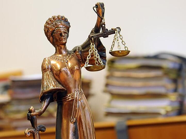 Eine goldfarbene Justitia-Figur steht vor Aktenbergen. Foto: Britta Pedersen/Archiv