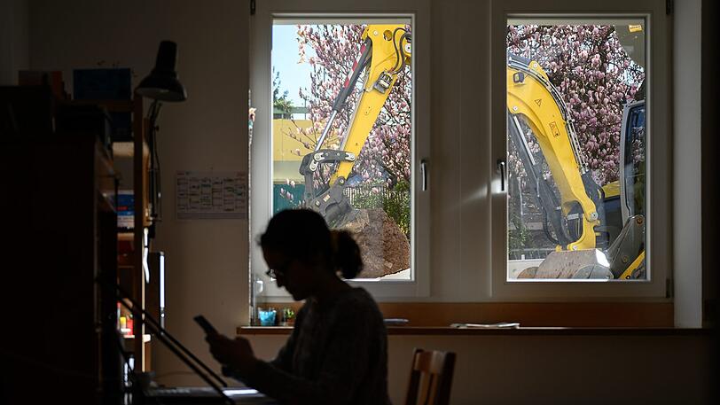Das strapaziert die Geduld, muss aber oftmals ausgehalten werden: Eine Frau arbeitet daheim, während vor ihrem Fenster ein Bagger werkelt.