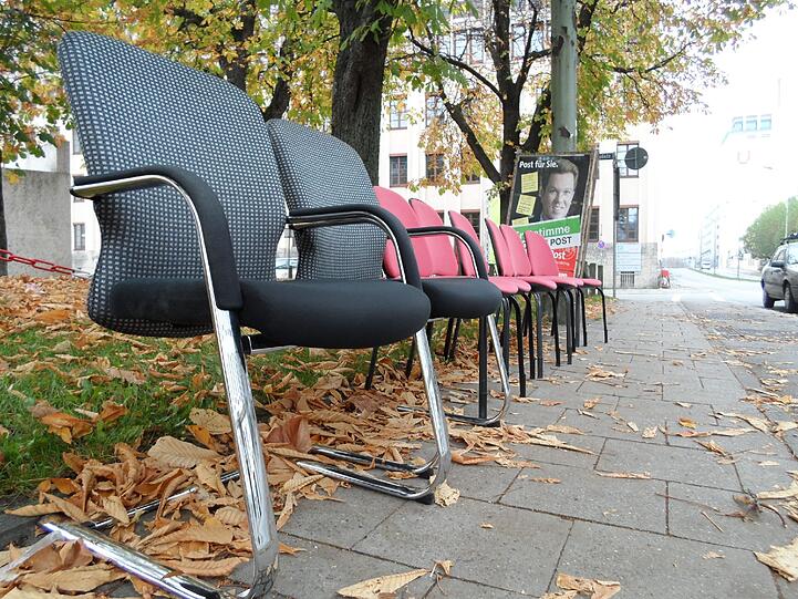 Zwei schwarz-graue uns sechs rote Stühle stehen am Rundfunkplatz aufgereiht. Dazu noch ein bisschen Geschirr. Und ein längst überfälliges Wahlplakat...