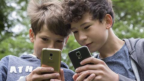 Zwei Buben zeigen sich gegenseitig etwas auf ihren Smartphones. (Symbolbild)
