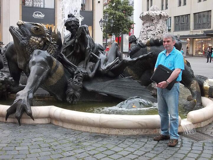 Er zeigt ein leicht verschmitztes Lächeln: Gustl Mollath vor dem Ehekarrusellbrunnen in Nürnberg. An das für die Frau des Dichters geschriebene Gedicht "Das bittersüße eh'lich' Leben" von Hans Sachs angelehnt, zeigt der Brunnen in sechs  Figurengruppen bildhaft überzeichnet die unterschiedlichen Szenen aus dem Auf und Ab des Ehelebens.