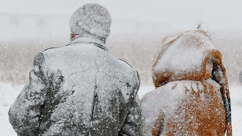 Winter in Bayern: Völlig mit Schnee bedeckt stehen zwei Zuschauer eines Pferdeschlittenrennens in Rinchnach (Bayern) an der Strecke.