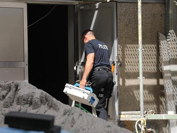 Ein Polizist geht mit einem Koffer in das Wohngebäude in der Kölner Innenstadt.
