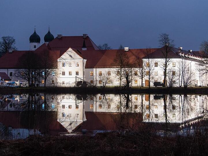 Das beleuchtete Kloster Seeon spiegelt sich im Wasser. Foto: Matthias Balk/dpa/Archivbild