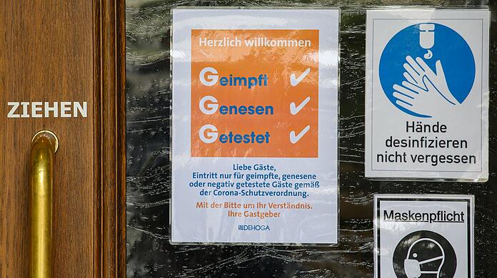 Schilder für die Einhaltung der 3G-Regel "Getest Geimpft Genesen", "Hände desinfizieren nicht vergessen" und "Maskenpflicht" kleben an der Tür eines Schankhauses. (Symbolbild)