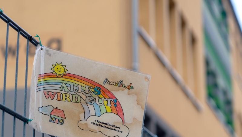 Ein Schild mit den Aufschriften "Alles wird gut!" und "#VereintImChaos" sowie "#WirBleibenZuhause" hängt am Zaun einer Grundschule. Ein Schild mit den Aufschriften "Alles wird gut!" und "#VereintImChaos" sowie "#WirBleibenZuhause" hängt am Zaun einer Grundschule.