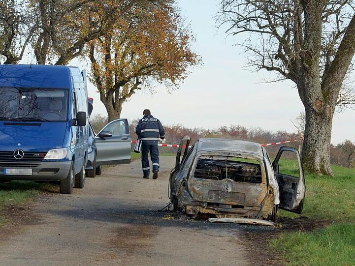 Polizisten stehen neben dem völlig ausgebrannten Fahrzeug außerhalb von Gerabronn.