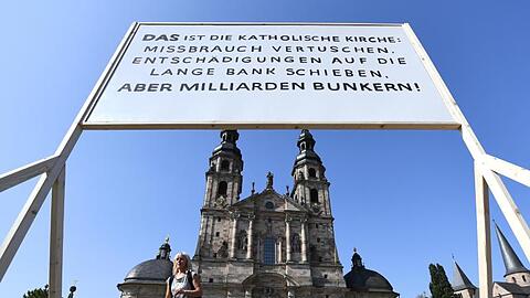 Ein Plakat der Giordano-Bruno-Stiftung mit der Aufschrift "DAS ist die Katholische Kirche: Missbrauch vertuschen. Entschädigungen auf die lange Bank schieben. Aber Milliarden bunkern !" steht am Rande der Herbstvollversammlung der Deutschen Bischofskonferenz auf dem Platz vor dem Dom.