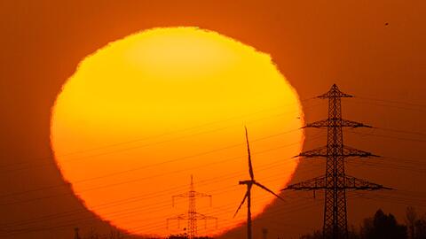 Die Sonne geht hinter Windrädern und Hochspannungsleitungen auf.