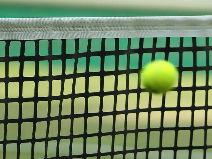 Ein Tennisball fliegt in ein Netz. Foto: picture alliance / Friso Gentsch/dpa/Symbolbild