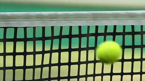 Ein Tennisball fliegt in ein Netz. Foto: picture alliance / Friso Gentsch/dpa/Symbolbild