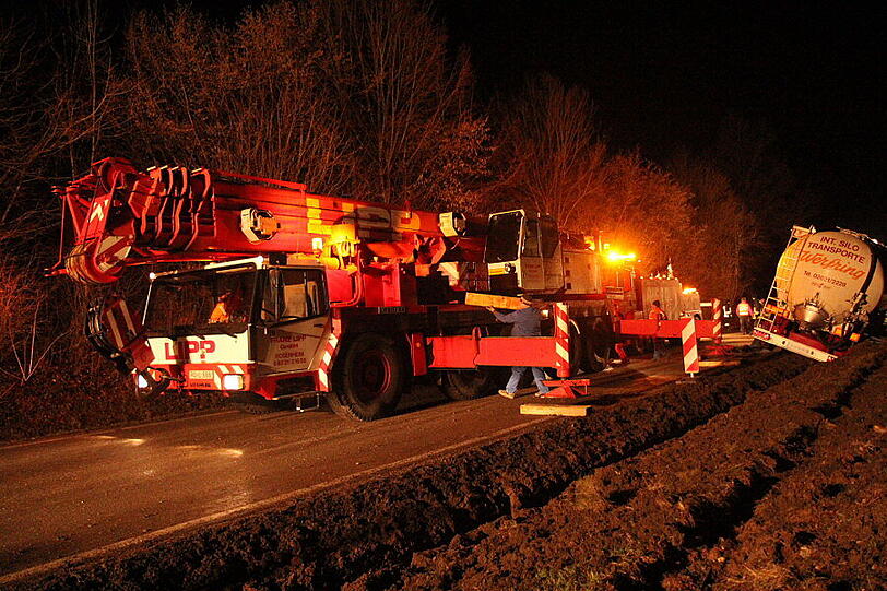 Ein Bergungsfahrzeug und zwei Kräne werden benötigt um den vollbeladenen LKW wieder auf die Straße zu ziehen.