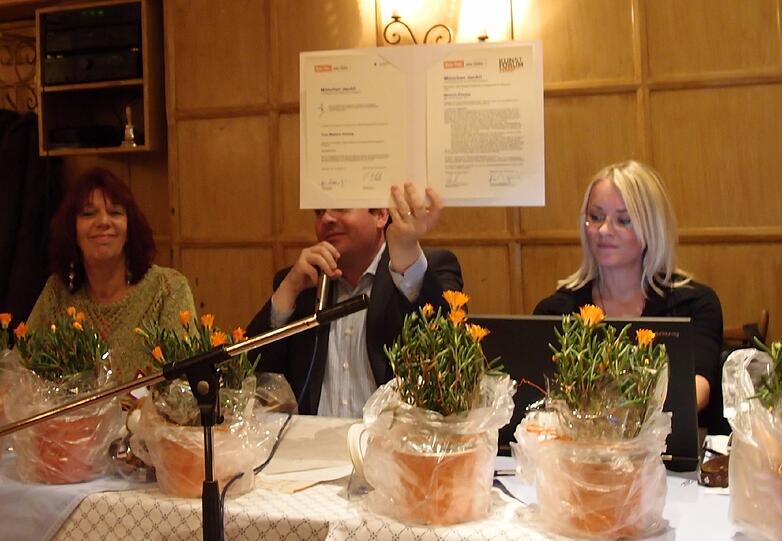 BA-Chef Clemens Baumgärtner hält die Urkunde für Melly Kieweg (links) und die Bürgerinitiative "Mehr Platz zum Leben" hoch.