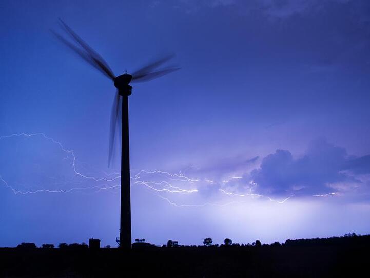 Blitze zucken am Horizont hinter einem Windrad. Foto: Julian Stratenschulte