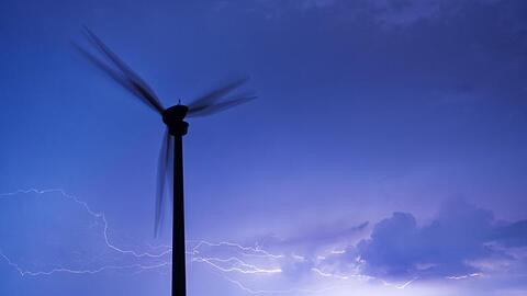 Blitze zucken am Horizont hinter einem Windrad. Foto: Julian Stratenschulte