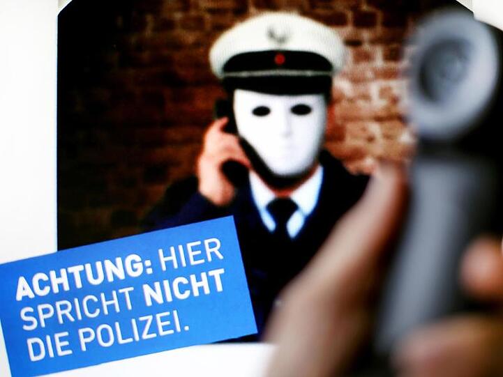 Ein Telefonhörer ist vor einem Plakat der Polizei NRW mit der Aufschrift "Achtung: Hier spricht NICHT die Polizei" zu sehen.