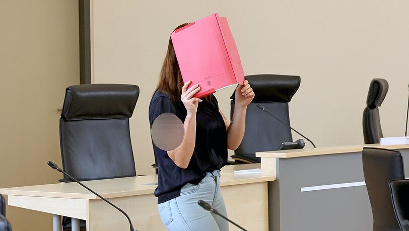 Die Angeklagte betritt den Gerichtssaal mit rotem Aktendeckel vor dem Gesicht.