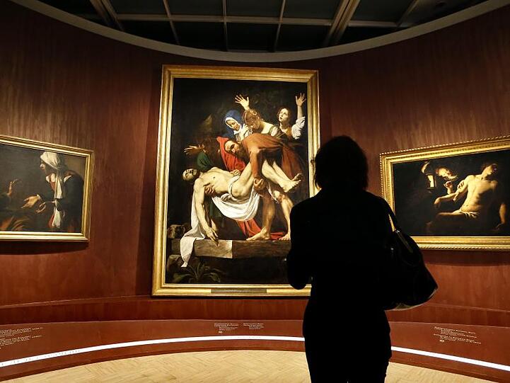Besucher betrachten das Bild "Die Grablegung Christi" von Michelangelo Merisi, bekannt als Caravaggio. Foto: Yuri Kochetkov/Archiv
