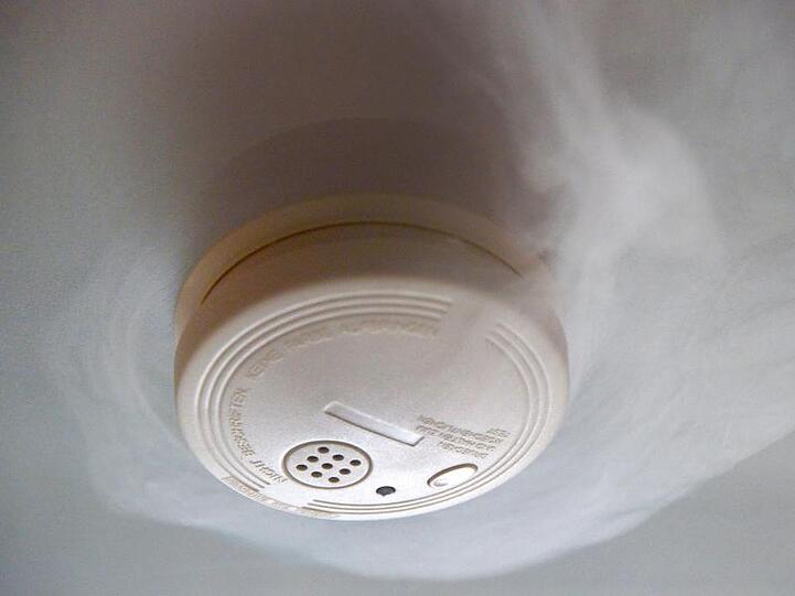 Ein Rauchmelder, umgeben von Rauch, hängt an einer Zimmerdecke. Foto: picture alliance / Peter Steffen/dpa/Symbolbild