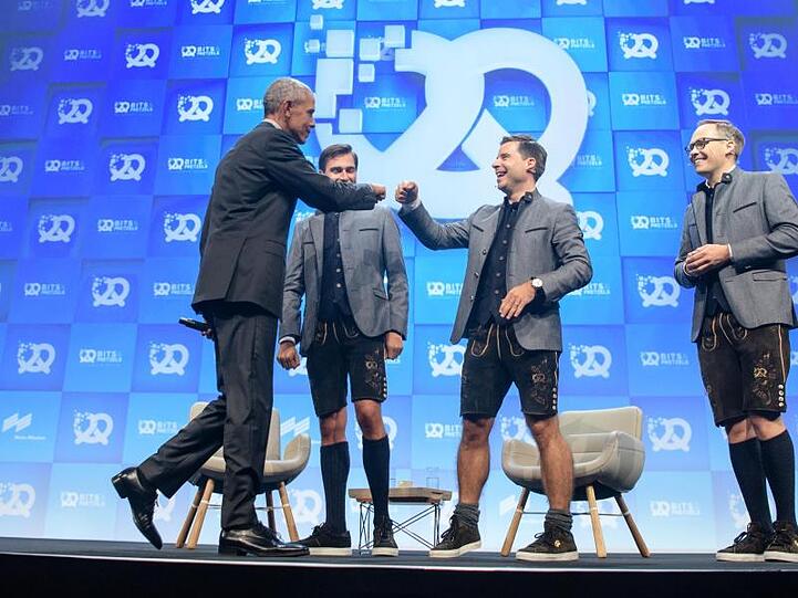 Barack Obama (l), ehemaliger Präsident der USA, begrüßt vor seiner Eröffnungsrede auf der Bühne drei Gründer. Foto: Matthias Balk