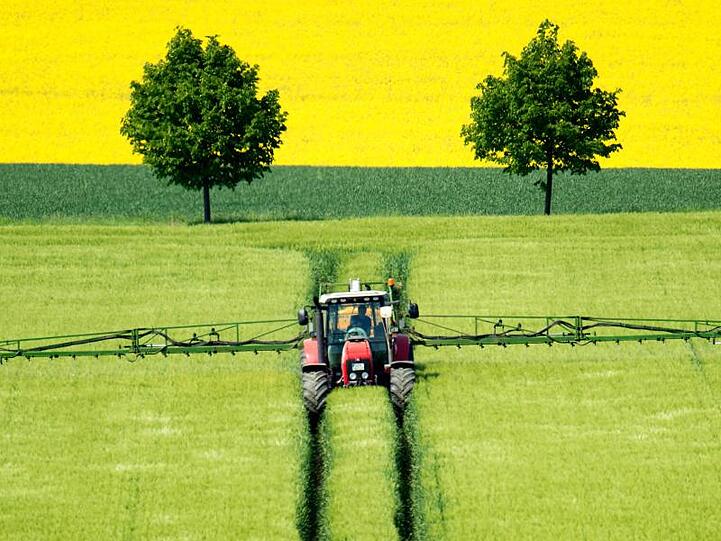 Ein Landwirt fährt mit einem Traktor über ein Gerstenfeld und versprüht Pflanzenschutzmittel.